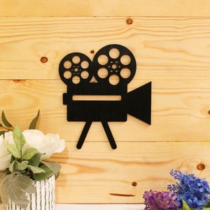 May include: Black silhouette of a vintage movie camera with two film reels on a light wood background.