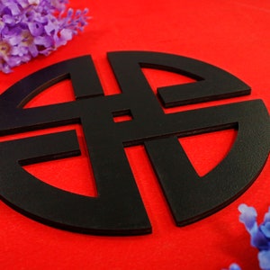 May include: A black wooden symbol with a circular shape and intricate knot design. The symbol is on a red background.