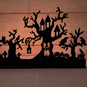 May include: Black silhouette of a haunted house with a spooky tree, crows, and tombstones. The silhouette is made of wood and is perfect for Halloween decor.