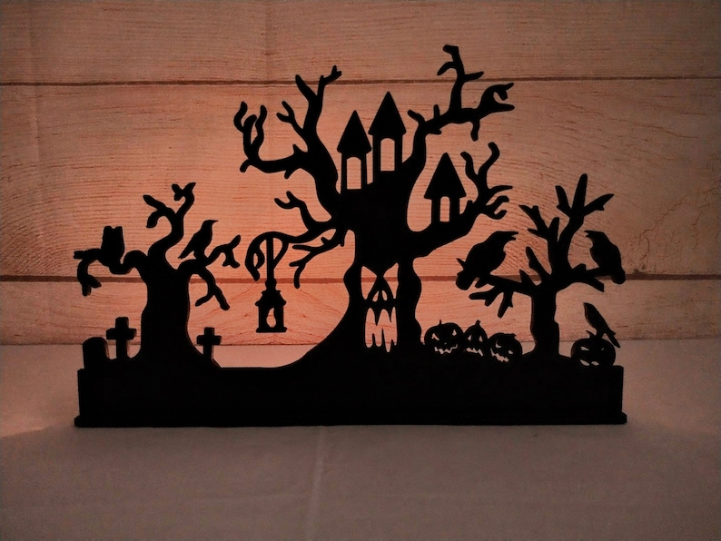 May include: Black silhouette of a haunted house with a spooky tree, crows, and tombstones. The silhouette is made of wood and is perfect for Halloween decor.