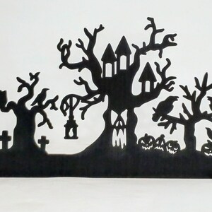 May include: Black silhouette of a haunted house with a tree growing out of it, two other trees with crows, and a graveyard with tombstones. The silhouette is on a black stand.