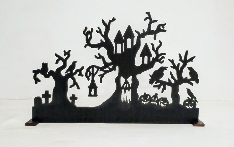 May include: Black silhouette of a haunted house with a tree growing out of it, two other trees with crows, and a graveyard with tombstones. The silhouette is on a black stand.
