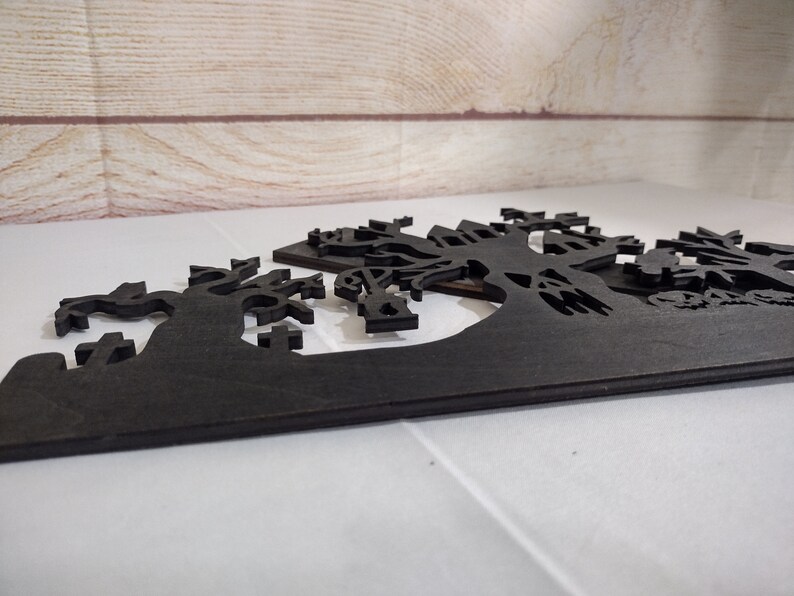 May include: Black wooden Halloween decoration with a spooky silhouette of a haunted house, trees, and a graveyard.