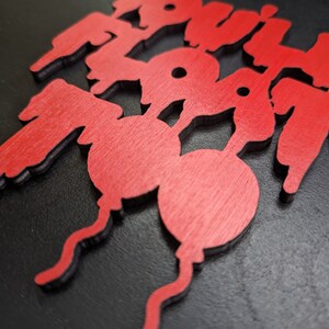 May include: Red wooden cutouts spelling out the word "BOOM" in a stylized font. The letters are layered, with a black outline. The "O"s are designed as balloons with curly strings.