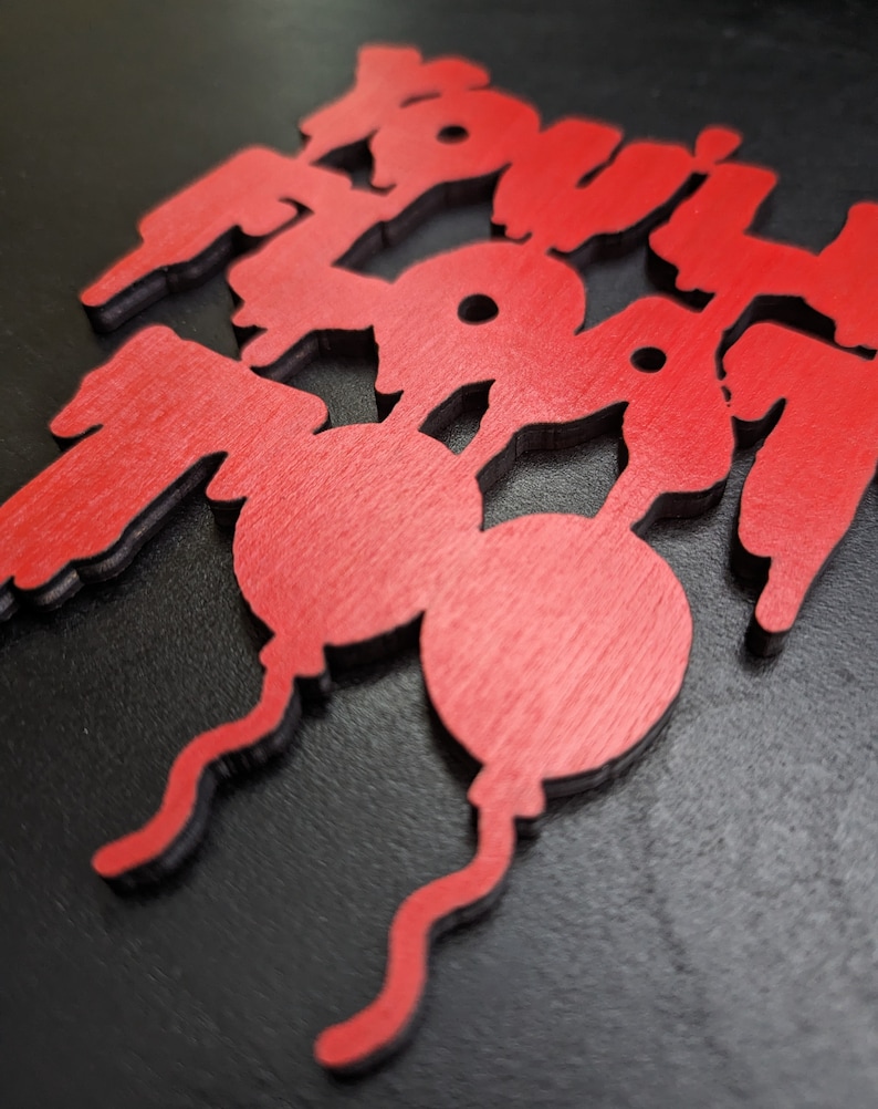 May include: Red wooden cutouts spelling out the word "BOOM" in a stylized font. The letters are layered, with a black outline. The "O"s are designed as balloons with curly strings.