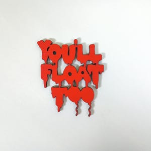 May include: A red wooden sign with the phrase "YOU'LL FLOAT TOO" in a dripping, stylized font. The sign has a white background and features a balloon design.