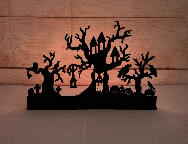 May include: Black silhouette of a haunted house with a tree, crows, and a graveyard. The house has windows and a door. The tree has branches and leaves. The crows are perched on the branches. The graveyard has tombstones and a lantern.