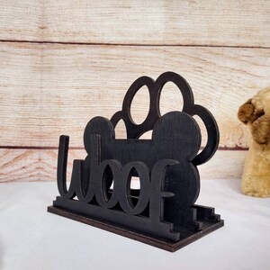 May include: Black wooden napkin holder with a paw print design and the word "woof" cut out.