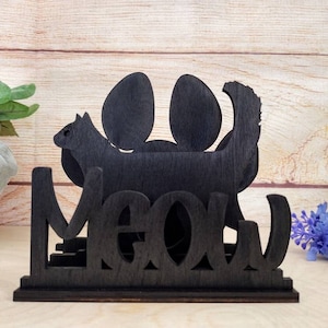 May include: Black wooden napkin holder with a silhouette of a cat and the word "Meow" in a stylized font.