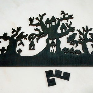 May include: Black wooden Halloween silhouette of a haunted house with trees, pumpkins, and a graveyard. The silhouette is cut out of a single piece of wood.