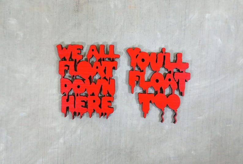May include: Two red wooden signs with the phrases "WE ALL FLOAT DOWN HERE" and "YOU'LL FLOAT TOO" in a dripping font. The signs are set against a gray, textured background.