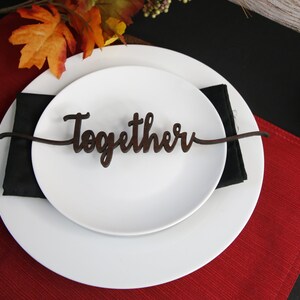 May include: A white plate with a black napkin and a wooden sign that says "Together" on a red placemat.