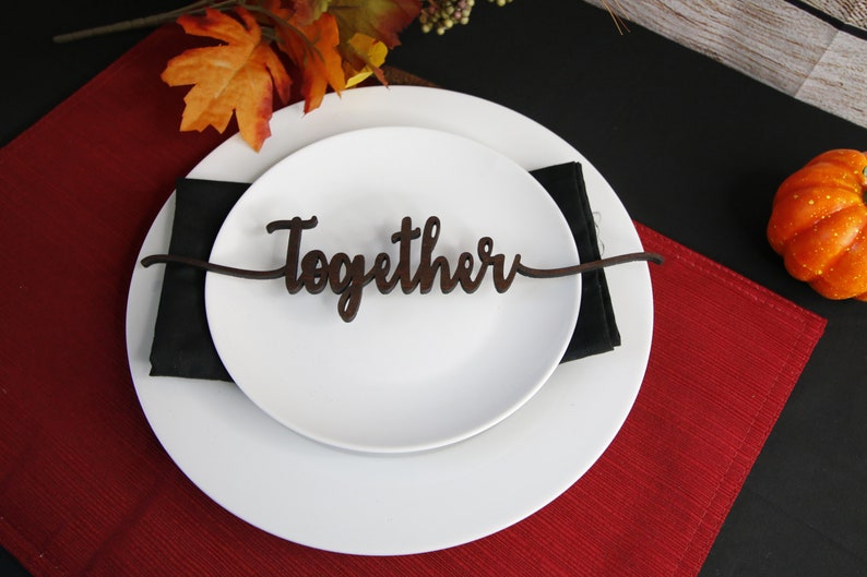 May include: A white plate with a black napkin and a wooden sign that says "Together" on a red placemat.