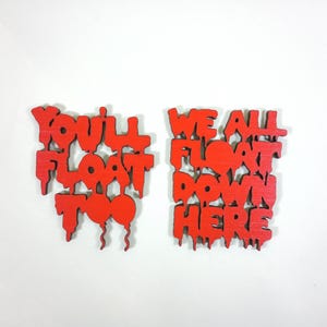 May include: Two red wooden signs with the phrases "YOU'LL FLOAT TOO" and "WE ALL FLOAT DOWN HERE" in a dripping font. The signs are on a white background.