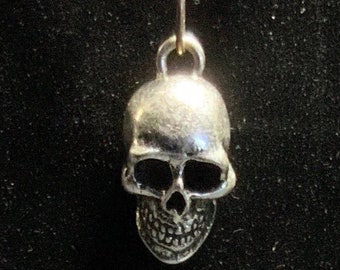 May include: A silver skull pendant necklace with a black cord. The necklace features wooden beads and silver-toned metal accents. The skull pendant is detailed with eye sockets, a nose cavity, and teeth.