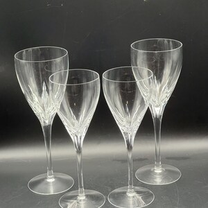 May include: Four clear crystal champagne flutes. The glasses have a tall, slender stem and a wide, round base. The bowl of each glass is elongated and tapers towards the top. The crystal has a decorative etched pattern. The glasses are arranged in a group.