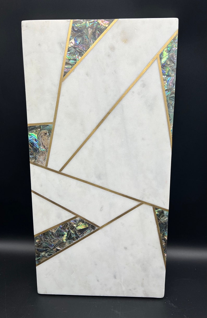 Op de afbeelding: Een rechthoekig decoratief stuk van wit marmer met een geometrisch ontwerp. Het ontwerp bevat goudkleurige lijnen en iriserende abalone schelp accenten. Het stuk heeft een gepolijste afwerking en een moderne esthetiek.