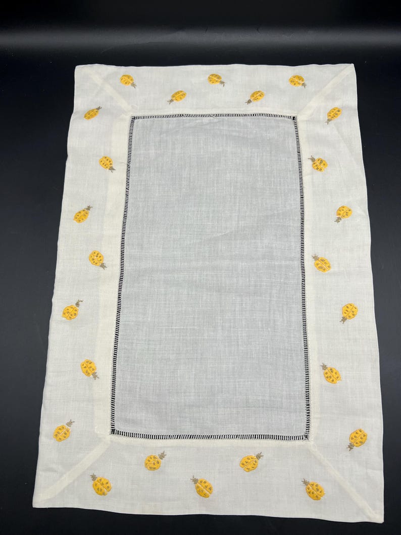 May include: White linen table runner with a yellow embroidered pineapple design around the border.