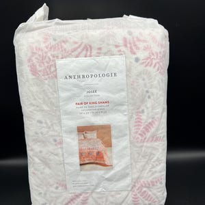 May include: A package of Anthropologie Josee Collection King Shams. The white fabric is patterned with pink and gray floral designs. The label reads "Pair of King Shams" and shows a picture of the shams.