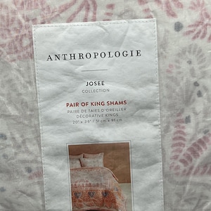 May include: A tag from Anthropologie for a pair of king shams. The tag reads "JOSEE COLLECTION" and "PAIR OF KING SHAMS". The shams measure 20" x 36" (51 cm x 91 cm). The background shows a floral pattern.