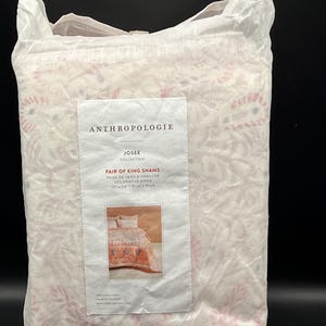 May include: A package of king shams from the Anthropolgie Josee Collection. The shams are in a white package with a floral pattern in pink and red. The label reads "Pair of King Shams" and "20 x 36 in / 51 cm x 91 cm."
