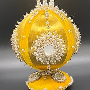 May include: A yellow velvet Christmas ornament with a beaded design and a white base.