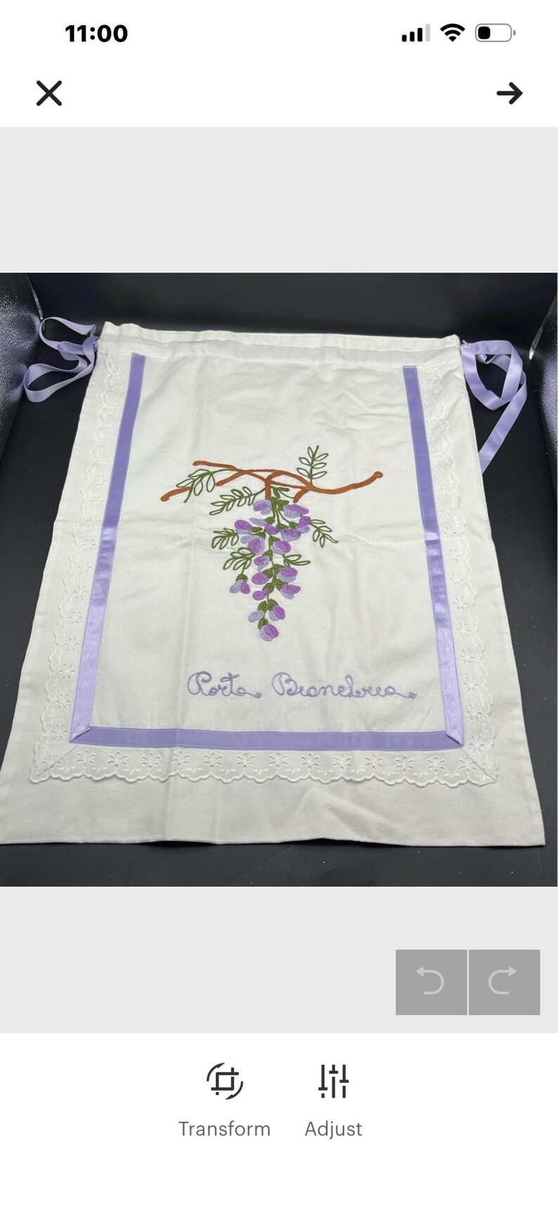 May include: White apron with a purple embroidered wisteria design and the text "Porto Branelva". The apron has a purple ribbon border and lace trim. The apron has purple ribbon ties.