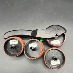 May include: A black Rollagraph stamp tool with four interchangeable stamp wheels. The wheels are brown with various patterns and text, including "Hedge Play," "Heart Angel," and "Spring Things." The tool is designed for crafting and scrapbooking.