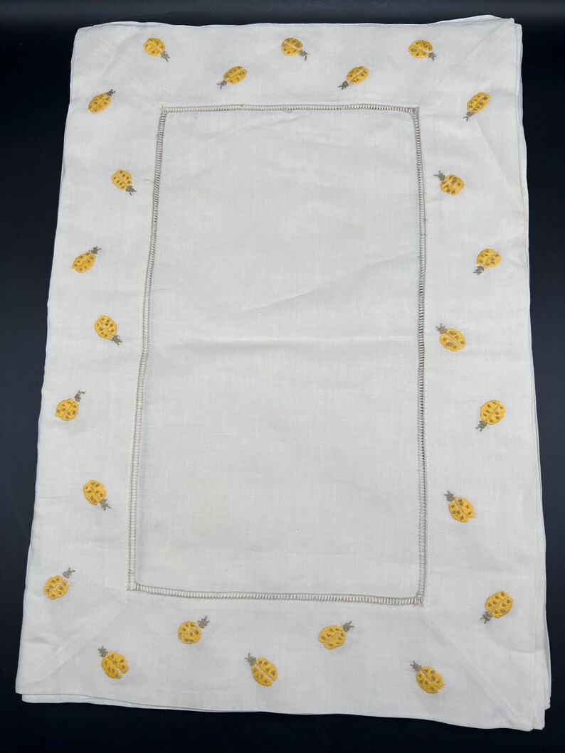 May include: A white linen tablecloth with a yellow pineapple embroidered border.
