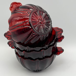 May include: Three red glass bowls with a scalloped edge and a decorative design on the bottom. The bowls are stacked on top of each other.