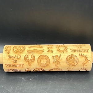 May include: A wooden rolling pin with a Game of Thrones theme. The rolling pin is engraved with the sigils of the different houses from the show, including the Starks, Lannisters, Targaryens, and Baratheons. The rolling pin also has the words "Game of Thrones" engraved on it.