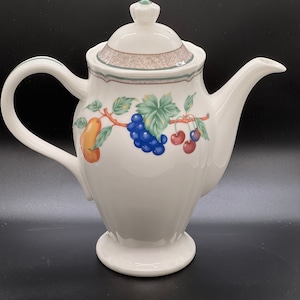 May include: White ceramic teapot with a green lid and a floral design featuring grapes, cherries, and pears.