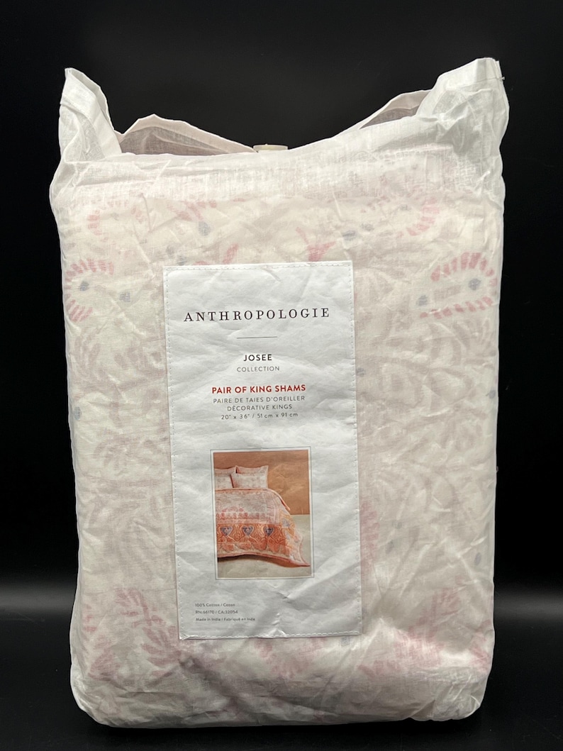 May include: A package of Anthropologie Josee Collection Pair of King Shams. The packaging is white with a floral pattern in pink and red. The label reads "Pair of King Shams" and shows a picture of the shams. The shams measure 20 x 36 inches.