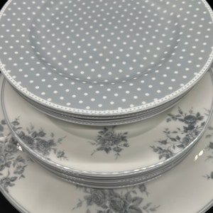 May include: A stack of white ceramic dinner plates with a gray and white polka dot design on the top plate and a gray floral pattern on the bottom plates.