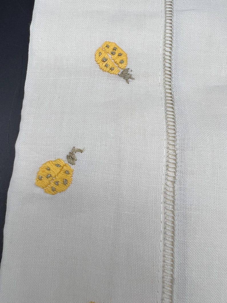 May include: White linen fabric with two embroidered yellow ladybugs with brown accents.