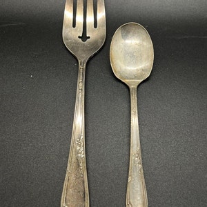 May include: A silver fork and spoon with ornate floral designs on the handles. The fork has a decorative cut-out in the center of the tines.