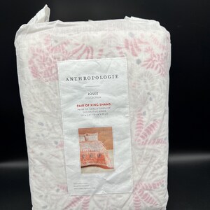 May include: A packaged set of Anthropologie Josee Collection King Shams. The white fabric features a pink floral pattern. The label reads "Pair of King Shams Decorative Kings" with dimensions of 20" x 36".