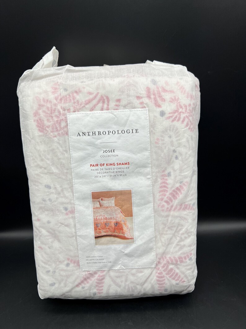 May include: A packaged set of Anthropologie Josee Collection King Shams. The white fabric features a pink floral pattern. The label reads "Pair of King Shams Decorative Kings" with dimensions of 20" x 36".