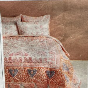May include: A bed set featuring a quilt and two pillowcases. The quilt has a floral pattern in shades of pink, red, and white, with a decorative border of hearts and paisley designs in orange and blue. The pillowcases match the quilt's design.
