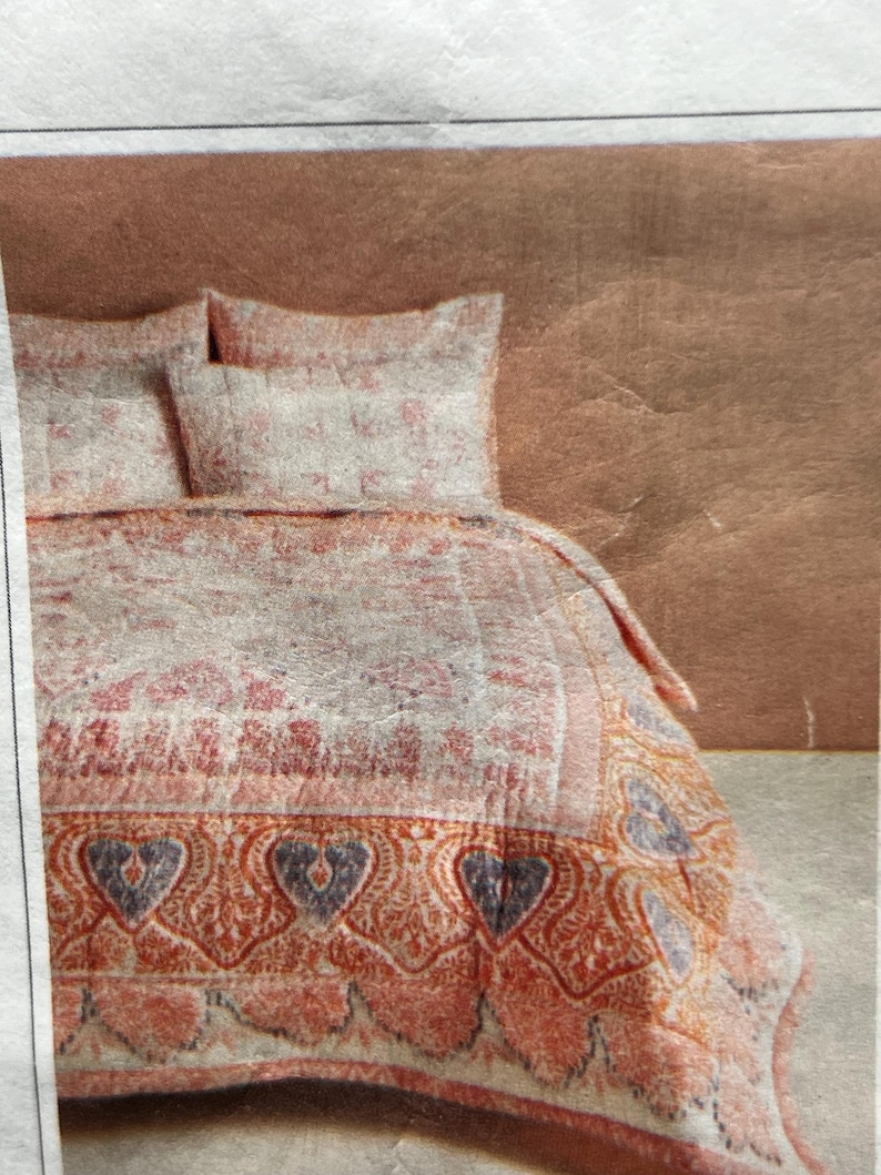 May include: A bed set featuring a quilt and two pillowcases. The quilt has a floral pattern in shades of pink, red, and white, with a decorative border of hearts and paisley designs in orange and blue. The pillowcases match the quilt's design.