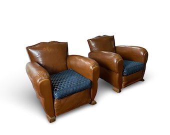May include: Two brown leather armchairs with blue patterned cushions. The chairs have a classic design with rounded arms and a slightly curved back.