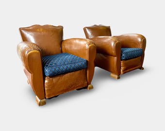 May include: Two brown leather armchairs with blue patterned cushions. The armchairs have a classic design with rounded backs and arms.