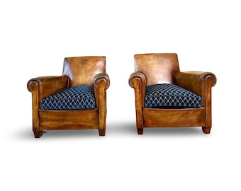 May include: A pair of brown leather armchairs with blue patterned fabric cushions. The chairs have rolled arms and a classic design.
