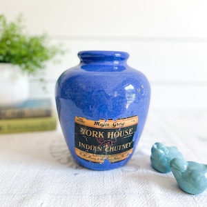 May include: A blue ceramic jar with a label that reads "Major Grey York House Indian Chutney" and a picture of a lion. The jar is sitting on a white tablecloth.