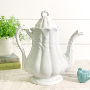 May include: White porcelain teapot with a floral design and a lid. The teapot has a bulbous body and a curved spout.