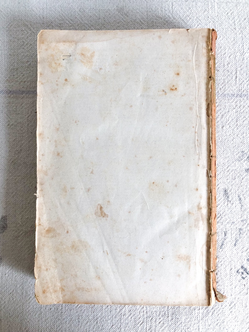May include: A vintage book with a white cover and a brown spine. The cover has several brown stains.