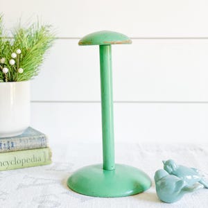 May include: A vintage green painted wooden hat stand with a round base and a mushroom-shaped top.