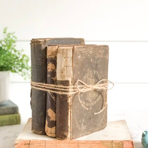 May include: A stack of three vintage hardcover books with brown covers and gold lettering. The top book is titled "Enquire Within Upon Everything" and has a small illustration of a building. The books are tied together with twine.