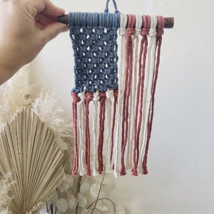 May include: A small, handmade American flag wall hanging made with blue, white, and red yarn. The flag is attached to a small wooden dowel.