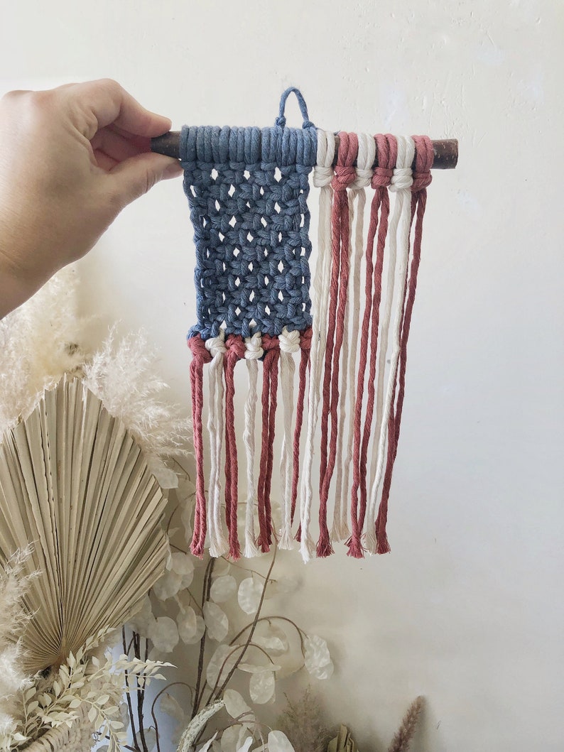 May include: A small, handmade American flag wall hanging made with blue, white, and red yarn. The flag is attached to a small wooden dowel.